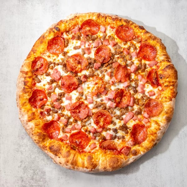 A whole meat lover's pizza, topped with pepperoni, sausage, and ham, on a light gray surface.