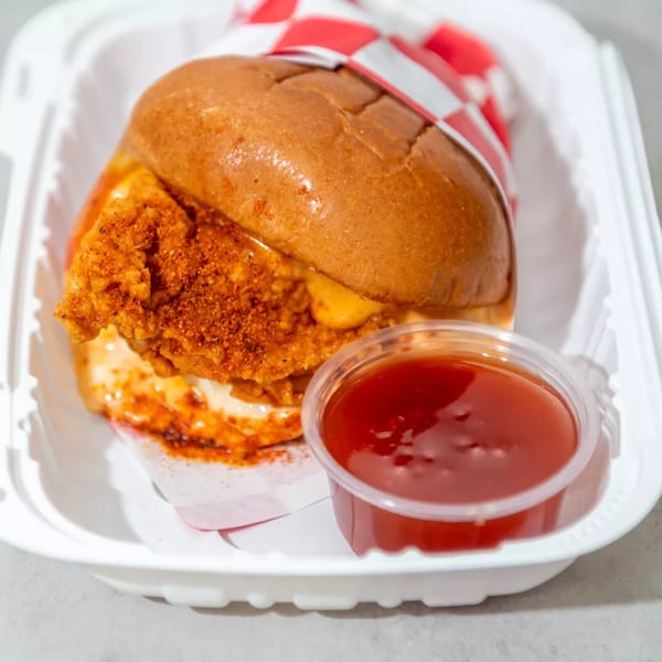 Spicy fried chicken sandwich with cheese and red sauce in a white takeout container.