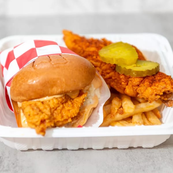 Spicy fried chicken sandwich, chicken tenders with pickles, and french fries in a white takeout container.
