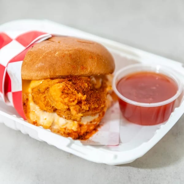 Spicy fried chicken sandwich with red and white checkered paper, served with a side of red sauce.