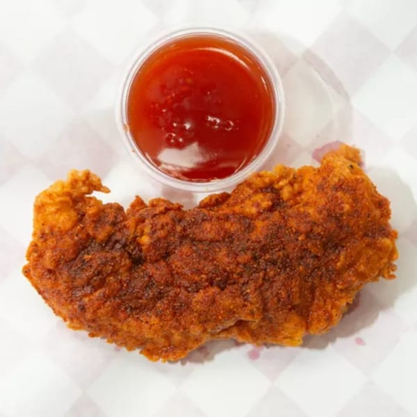 Crispy fried chicken tender with a side of red dipping sauce on a checkered paper.
