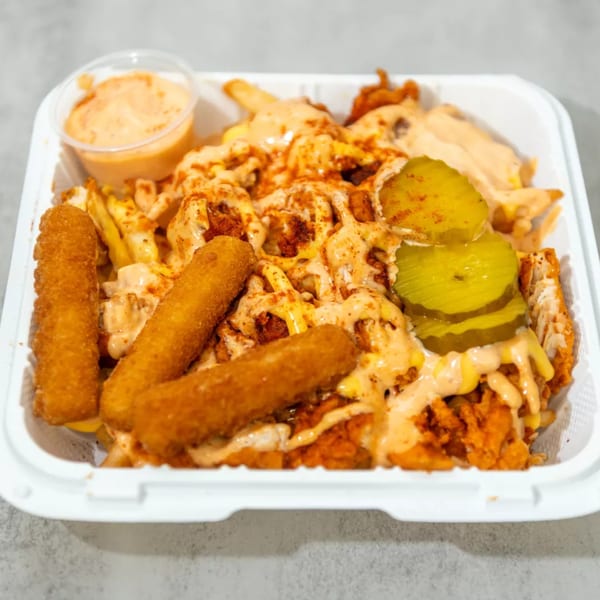 Loaded fries with fried chicken, cheese, sauce, pickles, and mozzarella sticks in a white container.