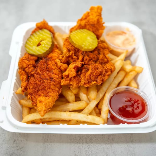Crispy fried chicken tenders with pickles and fries, served with ketchup and a creamy dipping sauce.